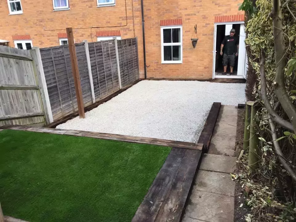 White Cotswald Stone area at the bottom of a sleeper walled artificial grass area with a path along the side.