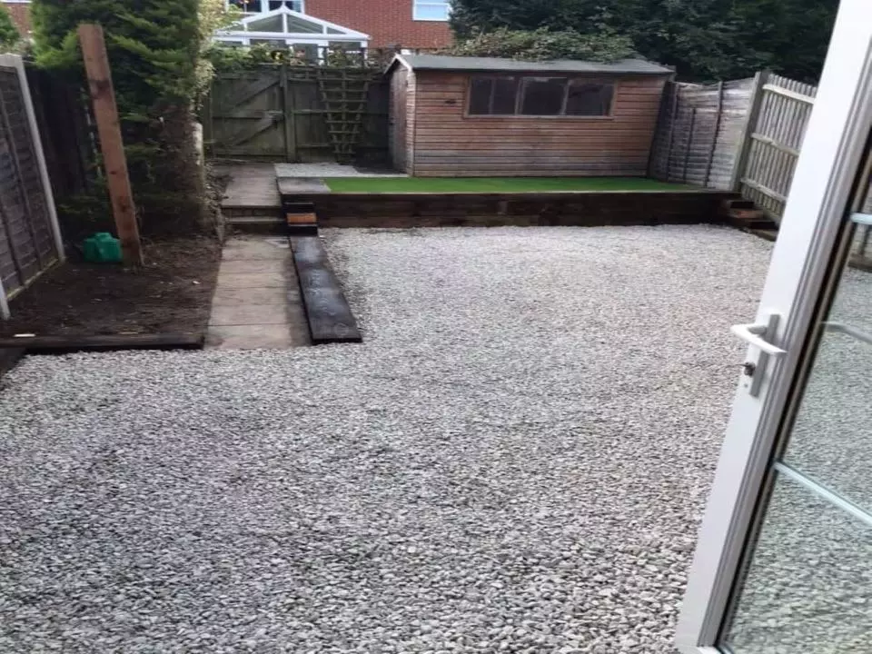 decorative stone area leading to a slabbed path with a few steps leading to a small artificial grass area and garden shed.