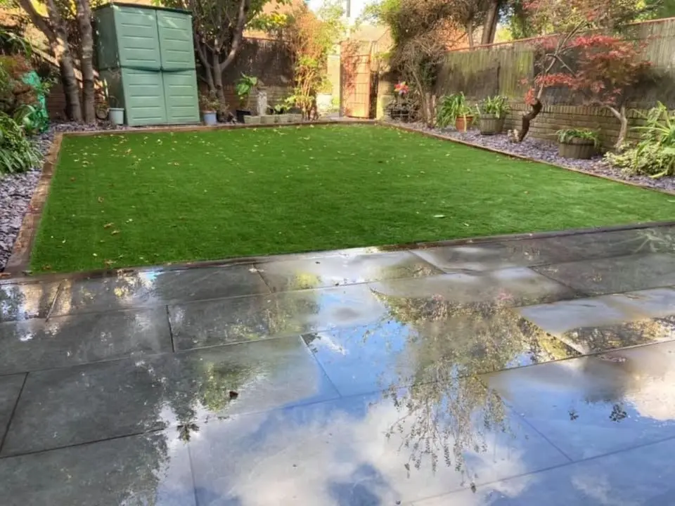 medium sized garden installed with decorative stones new slabbing area and artificial grass surrounded with a few trees and plants.