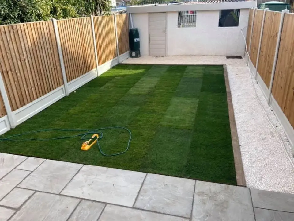 new turf lawn borderd by sleepers, decorative stones and a patio area at one end.